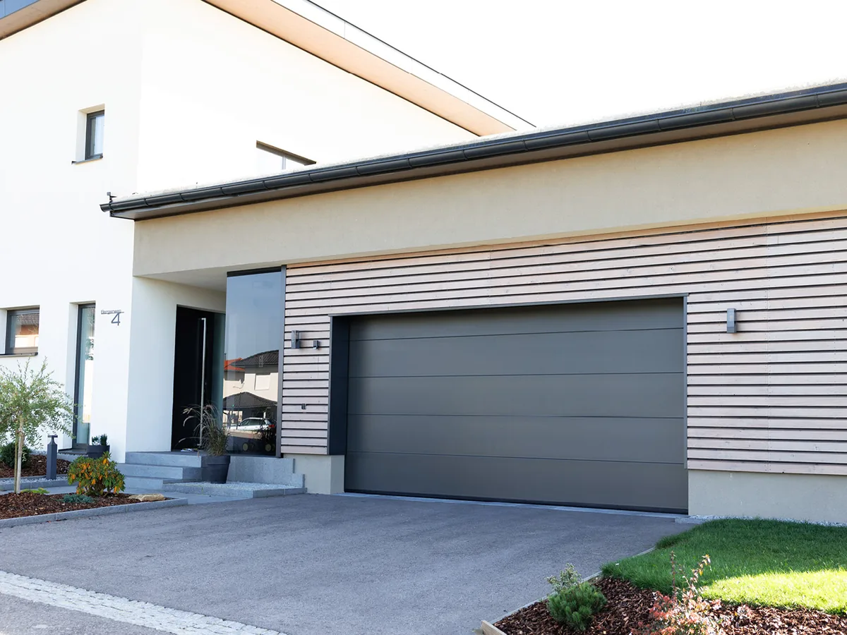 Normstahl Smart Sektionaltor in Anthrazitgrau an einer Garage mit Holzlattenfassade