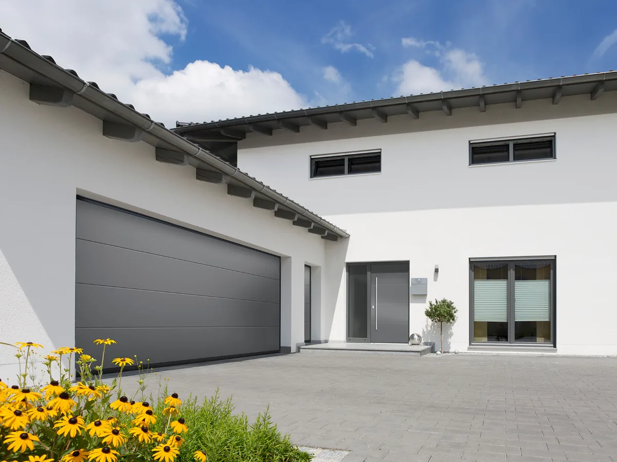 Normstahl Superior Sektionaltor in Graualuminium neben dem Hauseingang eines weißen Wohnhauses