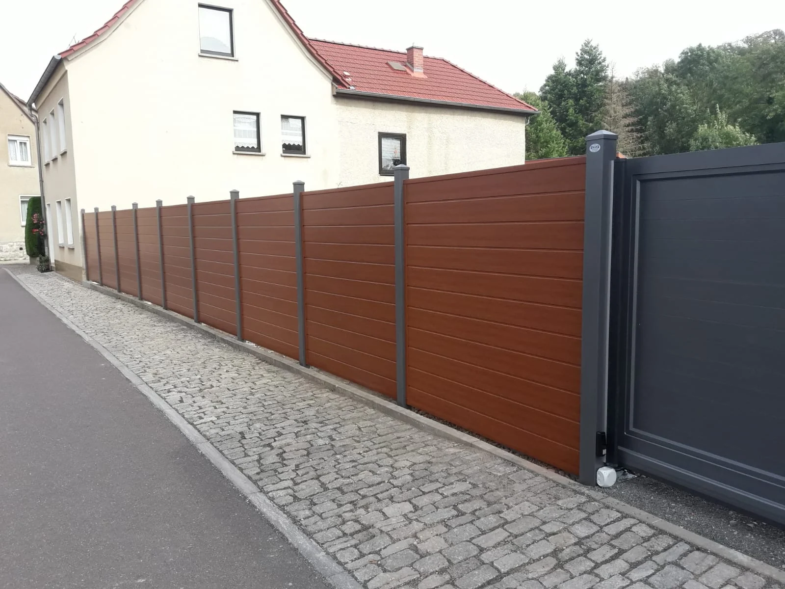 Sichtschutzanlage Salzburg in Holzoptik mit anthrazitfarbenem Schiebetor an einer Straße