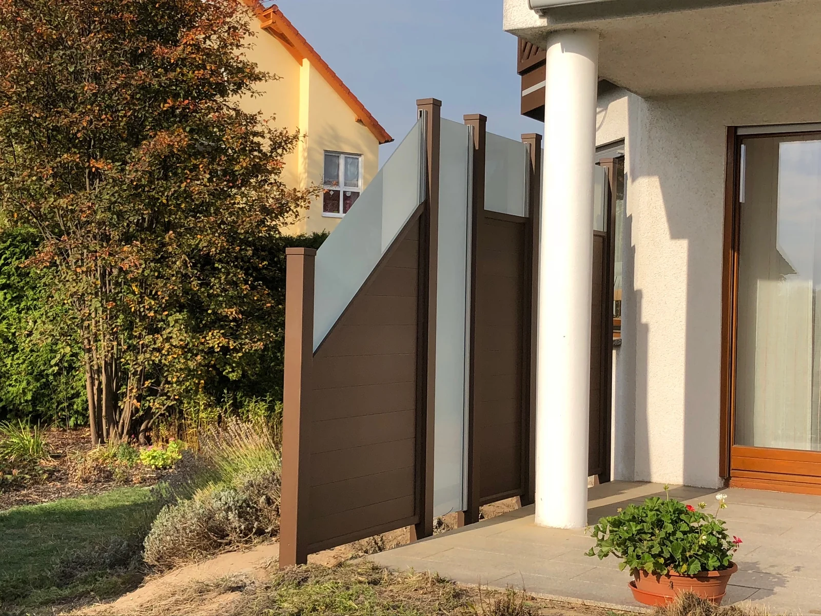 Sichtschutz Salzburg in Braun mit Glaseinsatz neben einer Terrasse